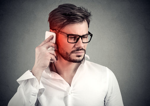 Man on the phone with headache. Upset unhappy guy talking on a cellphone on gray background. Negative emotion face expression