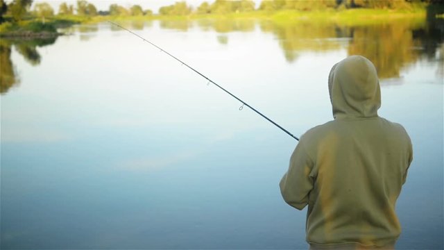 Fish-man fishing over the lake in the spring. Solitary angler staying alone surrounded by nature. He has a rest.