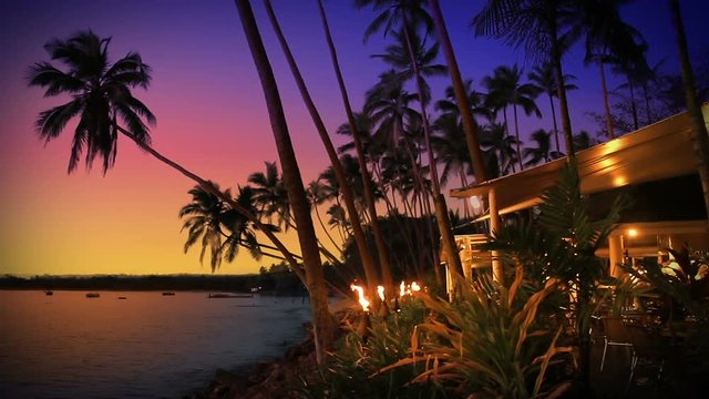Beach-side restaurant / cafe / bar lit by flaming torches, at sunset in tropical Fiji. Idyllic romantic summer night dining under a purple sky.