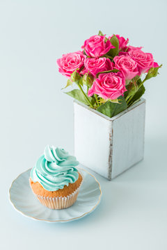 Blue pastel vertical banner with decorated with blue cream cupcake and bouquet of pink roses in retro shabby chic vase.