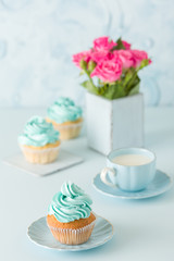 Blue pastel vertical banner with decorated cupcakes, cup of coffe with milk and bouquet of pink roses.