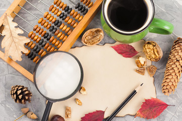 Old wooden abacus and full green cup of coffee and burnt blank paper and nut and leaves and cone of pine and magnifier and black pencil and acorn and chestnut on gray broken cement