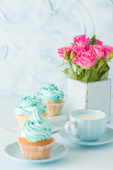 Blue pastel vertical banner with decorated cupcakes, cup of coffe with milk and bouquet of pink roses.