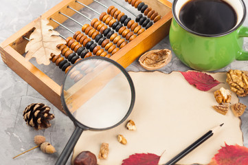 Old wooden abacus and full green cup of coffee and burnt blank paper and nut and leaves and cone of...