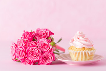 Cupcake with pink cream decoration and roses on pink pastel background.