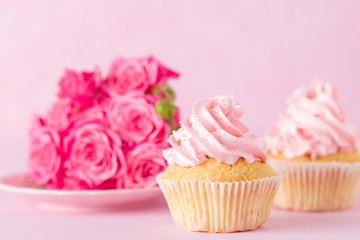 Cupcake with pink cream decoration and roses on pink pastel background.