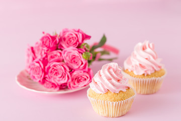 Cupcake with pink cream decoration and roses on pink pastel background.