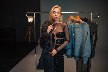Young woman stands next to rack with hangers and chooses fur coat.