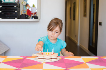 Obraz na płótnie Canvas three years old blonde child putting candles on birthday cake on colorful tablecloth at home 
