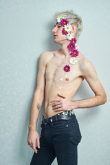 Beautiful aesthetic guy at the wall with flowers on the body