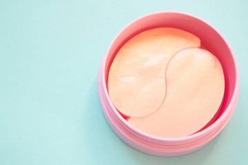 Golden pink hydrogel patches for eyes on blue background. Cosmetology, self-care, health care. Close up.