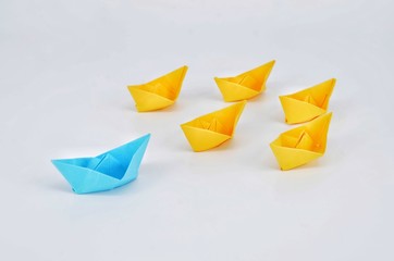 Leadership concept with a blue paper ship leading among yellow ships.