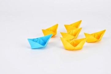 Leadership concept with a blue paper ship leading among yellow ships.