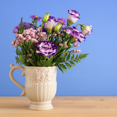 summer bouquet of purple flowers in the vase over wooden table and blue background.