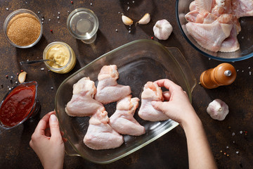 Hands put chicken wings in the baking dish. - 197516336