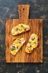 Toast with ham and mango on wooden Board, dark background, top view.