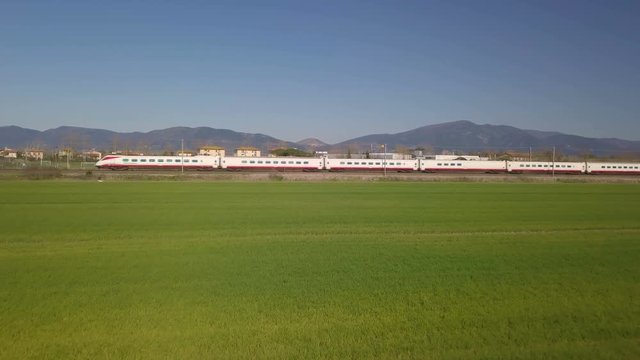 Treno bianco e rosso passeggeri in transito oltre un prato verde 