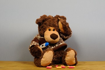 Teddy bear with thermometer on gray background.Person having temperature and headache. Bear Toy is ill.