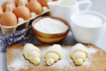Fototapeta na wymiar Baking Ingredients for Cooking Croissants. Dough, Eggs, White Sugar, Flour, Milk, Oil Butter. Preparation, Lavender Flowers. Kitchen Cuisine Table Grey Background, Homemade