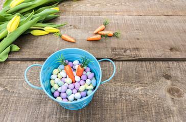 View from above of small blue bucket filled with candy eggs and carrots sitting on rustic wood