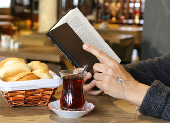 breakfast with tea and bread in a basket . Female read a book .