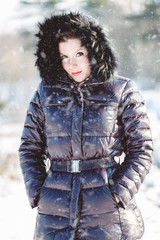 Pretty young stylish woman posing in a trendy fashion coat walks in the park on a sunny winter day