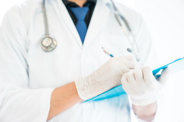 A doctor is working in the hospital, he is wearing a brown stethoscope and holding the clipboard for writing some notes.