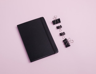 Composition of black stationery such as notebook and paperclips isolated on light pink background. Flat lay. Copy space. Top view