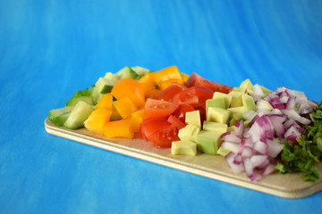 Chopped vegetables on a wooden board. Salad ingredients on blue background