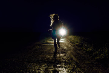 running female silhouette on a night country road running away from pursuers by car in the light of...