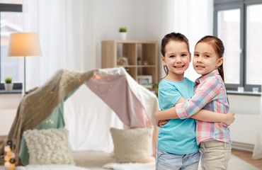 childhood, friendship and people concept - happy smiling little girls hugging at home over kids room and tepee background