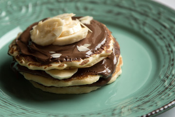 American pancakes with chocolate and banana on a green rustic plate