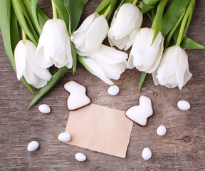 Happy Easter greeting card with white tulip and chocolate eggs and bunny, rustic background.