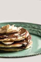 American pancakes with chocolate and banana on a pastel green rustic plate