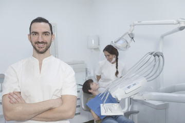 A portrait of a dentist with his team working in the background