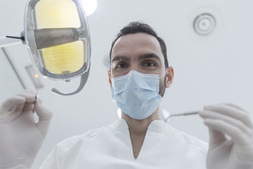 Naklejka premium Dentist wearing surgical mask while holding angled mirror and drill, ready to begin
