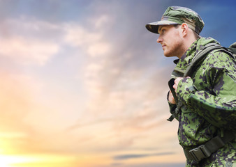 army, military service and people concept - young soldier or traveler in camouflage uniform with backpack hiking over sky background