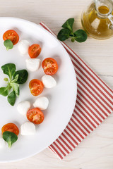 classic Italian Caprese salad with tomato cherry, salad corn on white plate. Textile decorated
