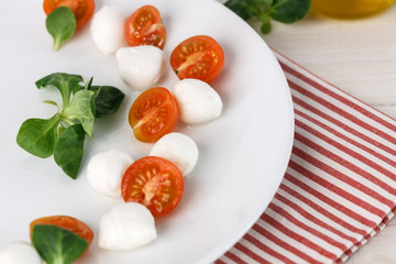classic Italian Caprese salad with tomato cherry, salad corn on white plate. Textile decorated