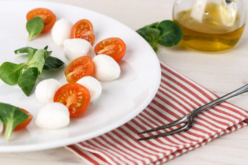 classic Italian Caprese salad with tomato cherry, salad corn on white plate. Textile decorated