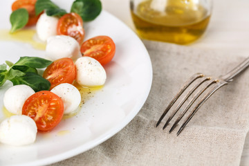 classic Italian Caprese salad with tomato cherry, salad corn on white plate. Textile decorated