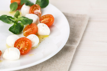 classic Italian Caprese salad with tomato cherry, salad corn on white plate. Textile decorated