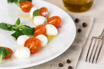 classic Italian Caprese salad with tomato cherry, salad corn on white plate. Textile decorated