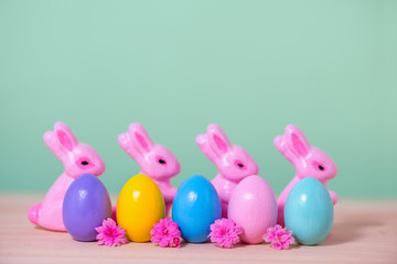 row multi colored painted Easter eggs, pink Bunnies and flowers over green background, holiday background