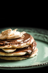 American pancakes with chocolate and banana on a pastel green rustic with black background plate