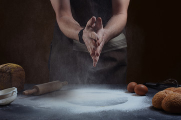 hand clap of chef with wooden rolling pin and  baking utensils with splash flour on dark background.