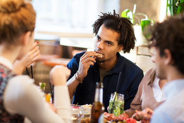 leisure, food and people concept - man with friends eating at restaurant