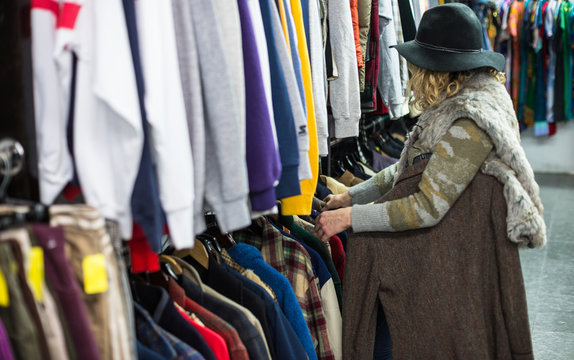 Woman in a hat browsing through clothing in a vintage thrift store