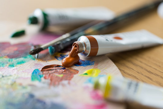 fine art, creativity, painting and artistic tools concept - close up of acrylic color or paint tubes, palette and brushes