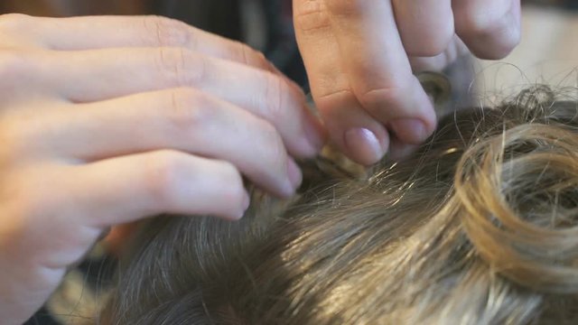 Stylist makes the curls to an attractive brown-haired using a lot of bobby pins. Close-up